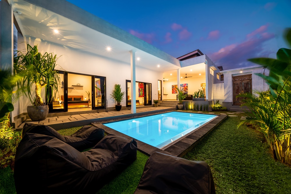 A modern outdoor pool area surrounded by plants, with bean bag chairs and a view of a stylish home at dusk - Cal-West Property Inspections A modern outdoor pool area surrounded by plants, with bean bag chairs and a view of a stylish home at dusk - Cal-West Property Inspections